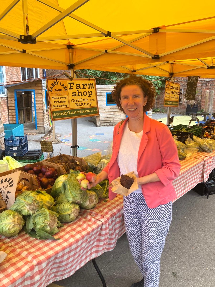 Anneliese next to a vegetable and fruit stand, holding a cake.