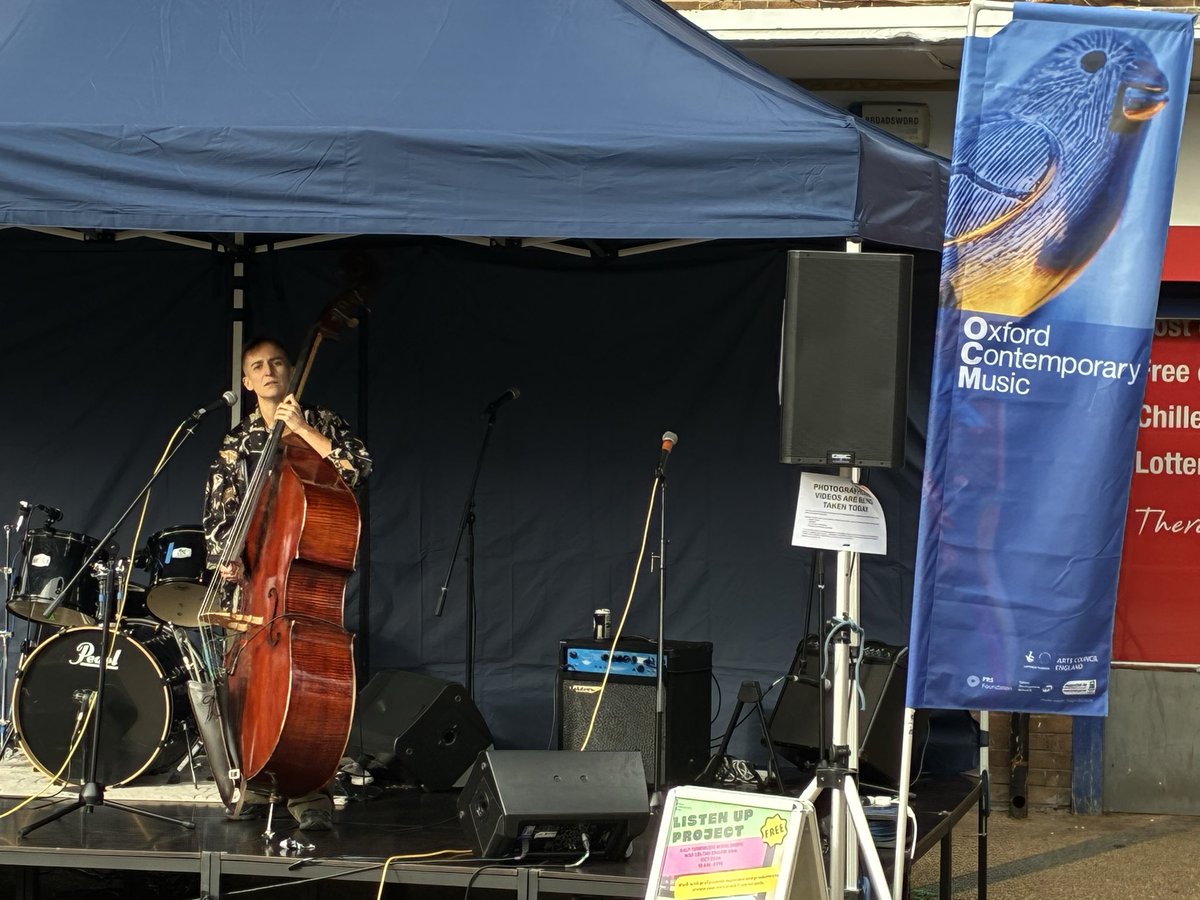 The artist Rocco on a stage with a double bass, with speakers in the background and an ‘oxford contemporary music’ flag next to the stage.