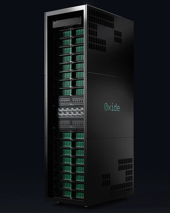 A tall black Oxide server rack against a dark background, viewed from the front-left with its front open, showing rows of compute sleds with green faceplates in the upper and lower sections and networking switches in the middle. The side panel has perforated ventilation patterns and a green Oxide logo.