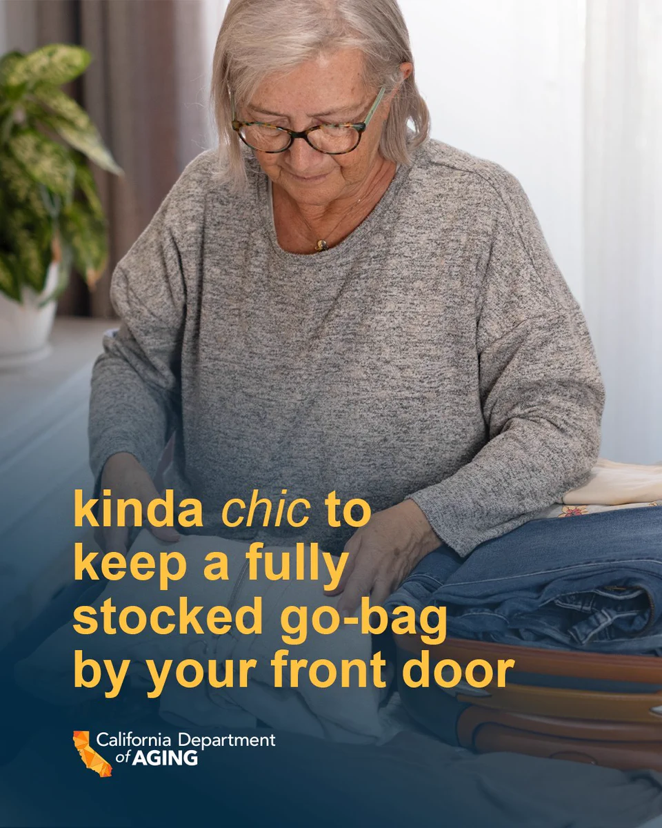 An individual with glasses is packing a suitcase, surrounded by folded clothes. The text on the image reads, "kinda chic to keep a fully stocked go-bag by your front door." The logo of the California Department of Aging is at the bottom left corner.