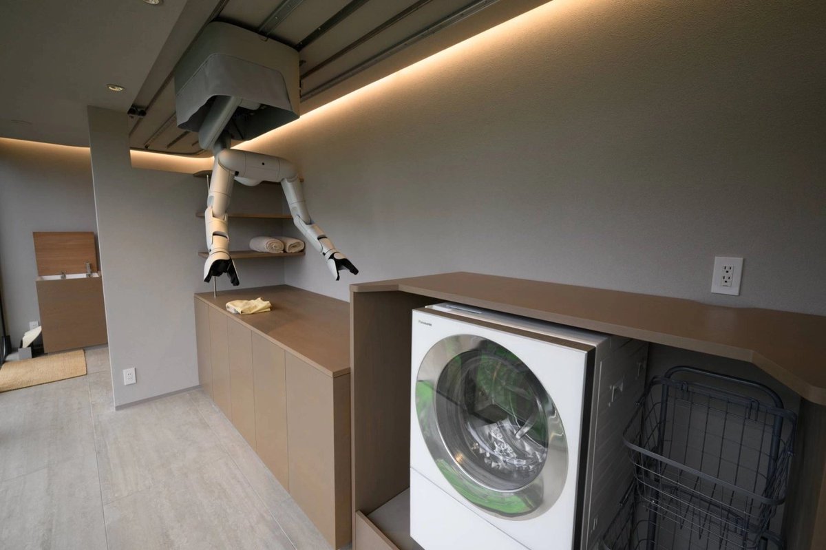 vigram_void's tweet photo. Tokyo startup MW unveiled a wonderfully contrarian approach to domestic robotics: robotic arms built directly into houses, traveling along ceiling-mounted rails rather than walking around on legs. In demonstrations, the system moved groceries, sorted food between pantry and refrigerator, handled laundry and folded a towel; MW wants its first robot-equipped homes on sale in Tokyo in 2028 and eventually targets 10,000 homes annually by 2035.

The company has raised roughly ¥3 billion (~$20M) so far.

I think this idea deserves far more attention than it will probably get.

Humanoids solve an extraordinarily difficult constraint:

Make the robot adapt to an environment designed for humans.

MW flips the problem:

Make the environment adapt to the robot.

A ceiling rail eliminates locomotion, stairs, balance and much of collision avoidance while supplying permanent power and known coordinates.

That could make a $20k fixed manipulator dramatically more useful than a $100k humanoid for many homes.

It's essentially the smart-home concept taken to its logical conclusion: the building itself becomes a robot.