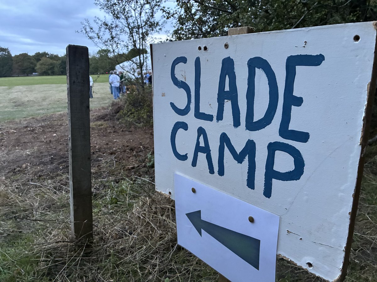 Sign with ‘Slade Camp’ painted onto it, next to an open field.