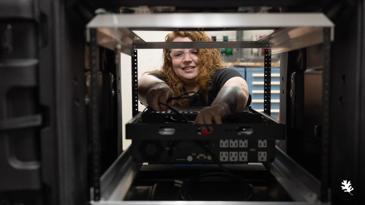 Christi Johnson, a technical staff member in ORNL's Multimodal Sensor Analytics Group, reaching into an equipment rack to install and connect a data acquisition system for a new project. 