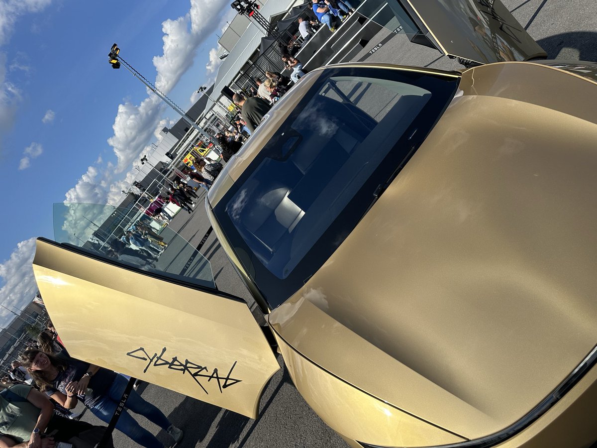 Roosie__'s tweet photo. Gold Cybercab at the Giga Brandenburg Summer Games.

Didn’t expect to walk past this today. The gold looks different in the sun than it does in pictures, and that CYBERCAB lettering on the hood is looks so cool! 

Doors up, people crowding around it, factory in the background. Still strange seeing it sitting here instead of on a screen.
Inside it’s almost empty compared to a normal car. Big screen, bench seats, no steering wheel on this one. 

Kids were more interested in the doors than anything else - Fair enough.

Pretty cool they actually brought one out for the event.

#tesla #cybercab #Ai #taxi #gold #goldenera #TSLA #germany #brandenburg #Future #autonomy
