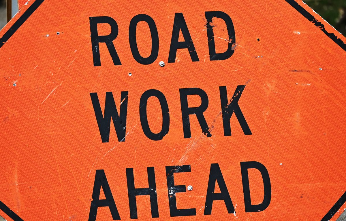 Orange diamond-shaped sign with bold black letters reading 'ROAD WORK AHEAD' indicating upcoming construction.