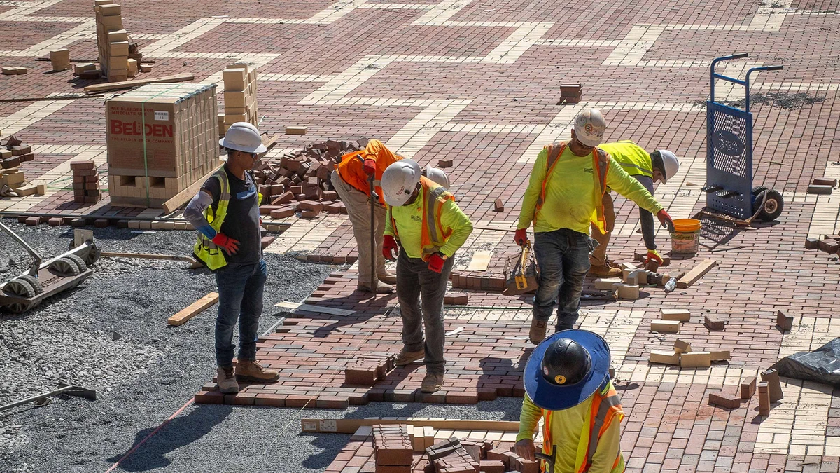 Construction workers laying red bricks to create a patterned pavement under bright daylight.