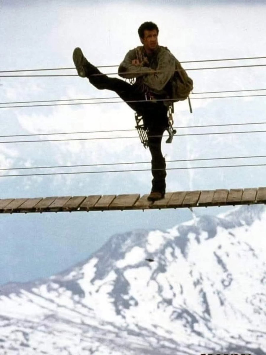 DaveBuzan's tweet photo. My fascination with "Cliffhanger" (1993) never ends! This ultra-rare production pic features Stallone stretching before a large stunt sequence. 

He's standing on the Ponte Cristallo--the longest bridge in the Dolomites--which is located at an elevation of 5547 feet. https://t.co/sY9B2jMcjw