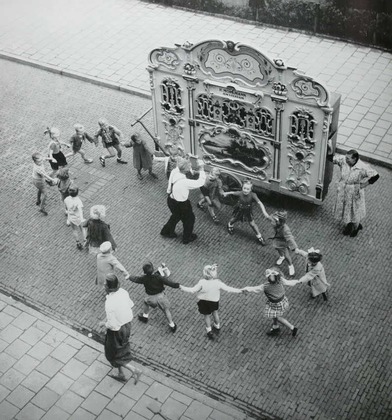 eyeonaxis's tweet photo. Children dancing in the street with an organ. Amsterdam, 1950s, by Henk Jonker

The street organ, called a "pierement" in Dutch, was a regular presence in Amsterdam's streets throughout the 20th century. It was pushed by hand from block to block, playing the favorite tones of the pierementman.