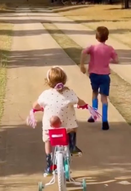 Lilibet on a bicycle with Archie running ahead