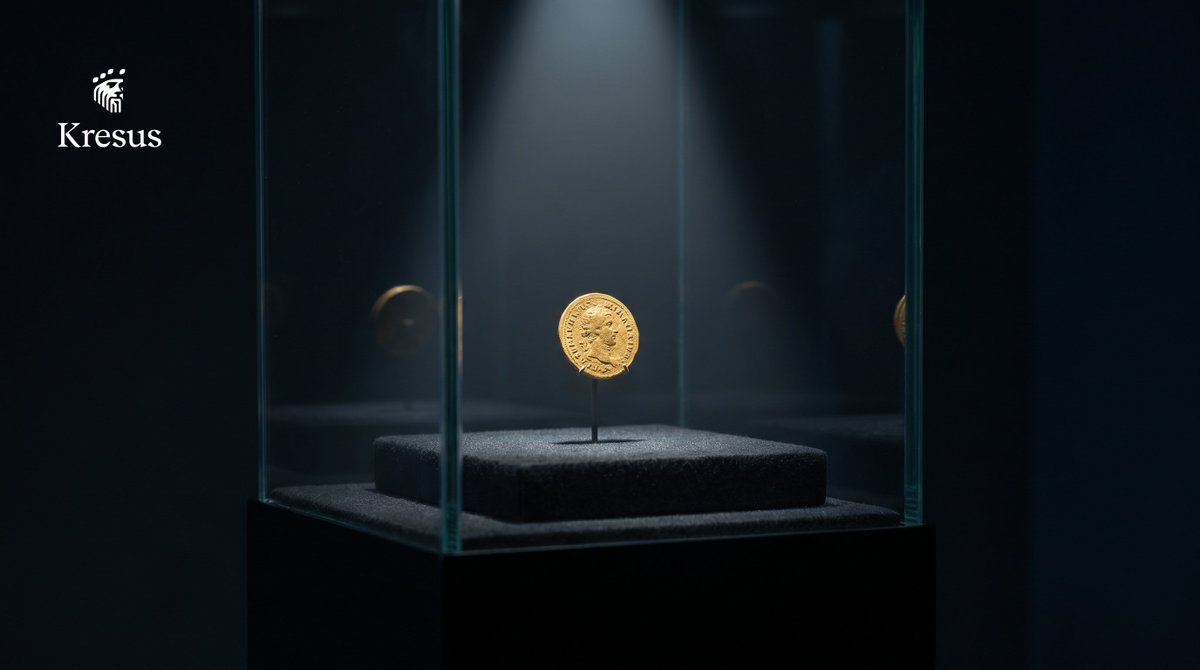 A single gold coin mounted inside a sealed glass museum display case under a spotlight in a dark gallery