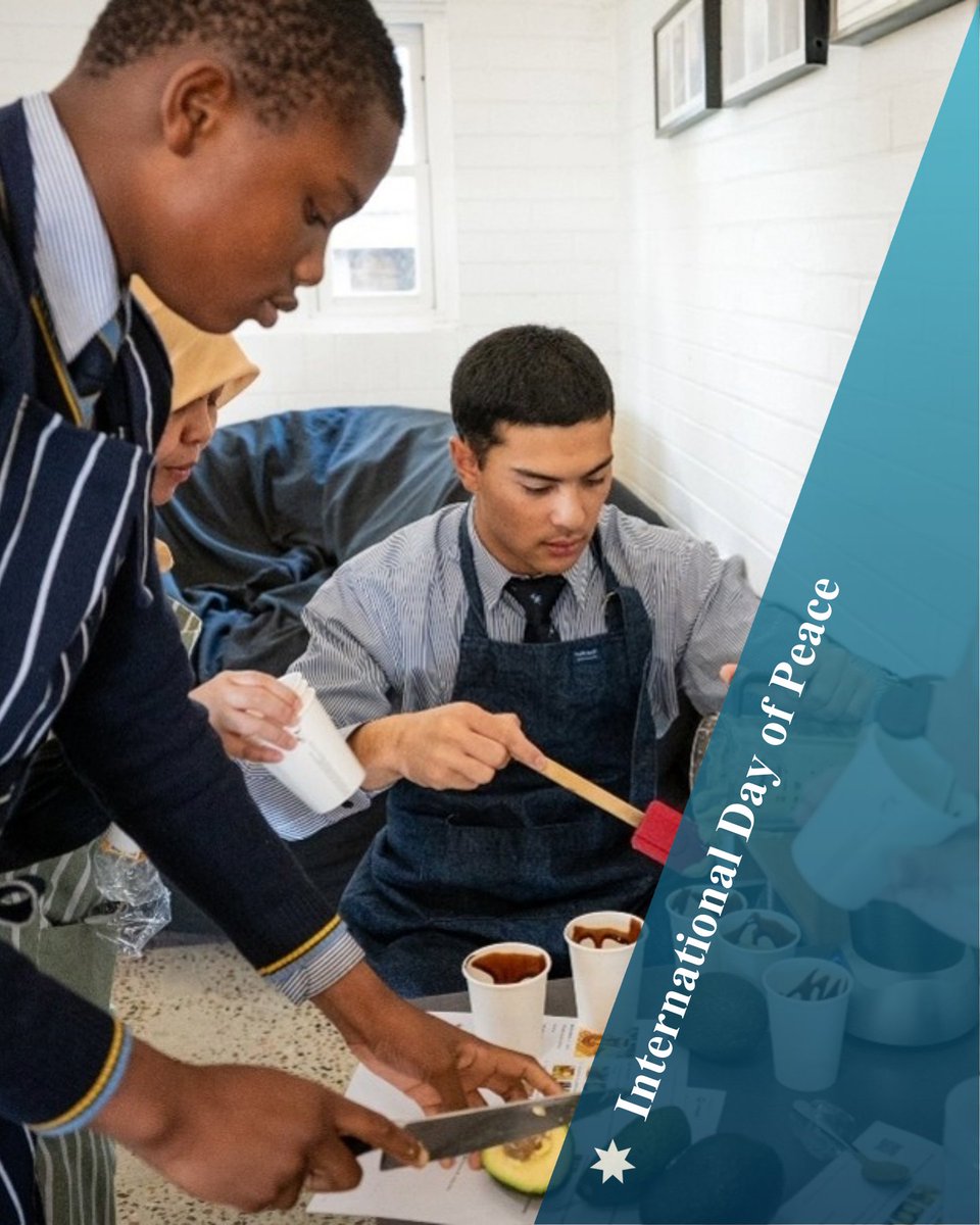Two students prepare food with an Indonesian lady wearing a jilbab with text: International Day of Peace.
