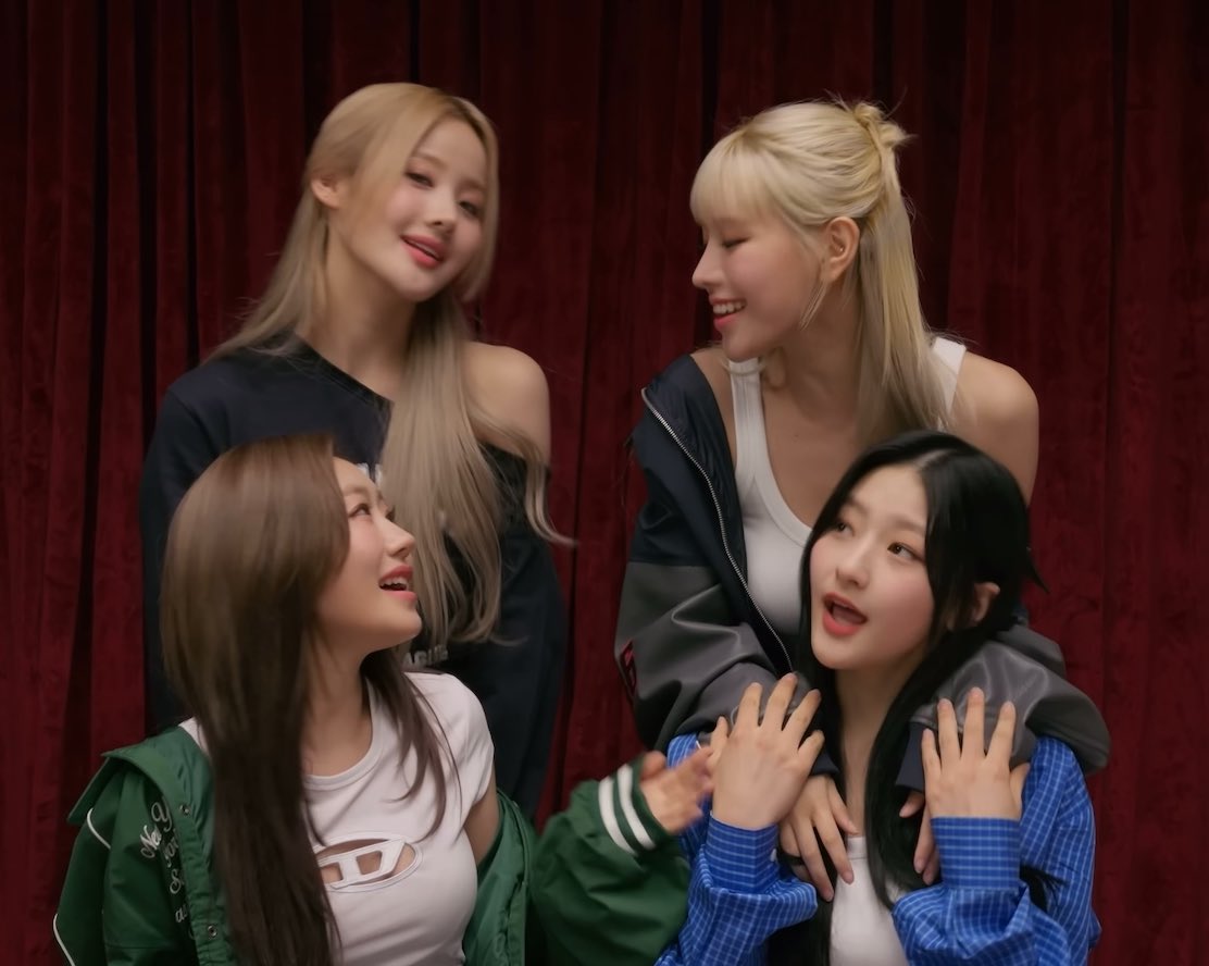 Four members of the K-pop group BLACKPINK posing together against a red curtain background, smiling and laughing.