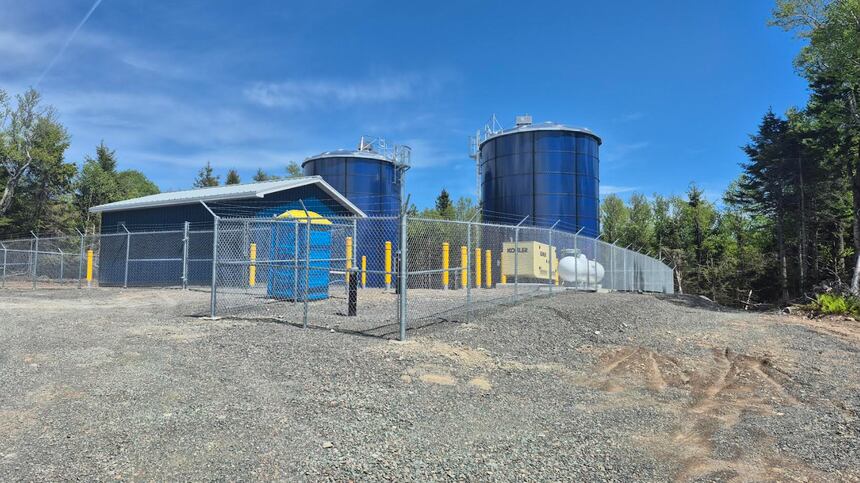 An industrial water treatment facility featuring two large blue cylindrical tanks and a small blue building in a fenced perimeter.
