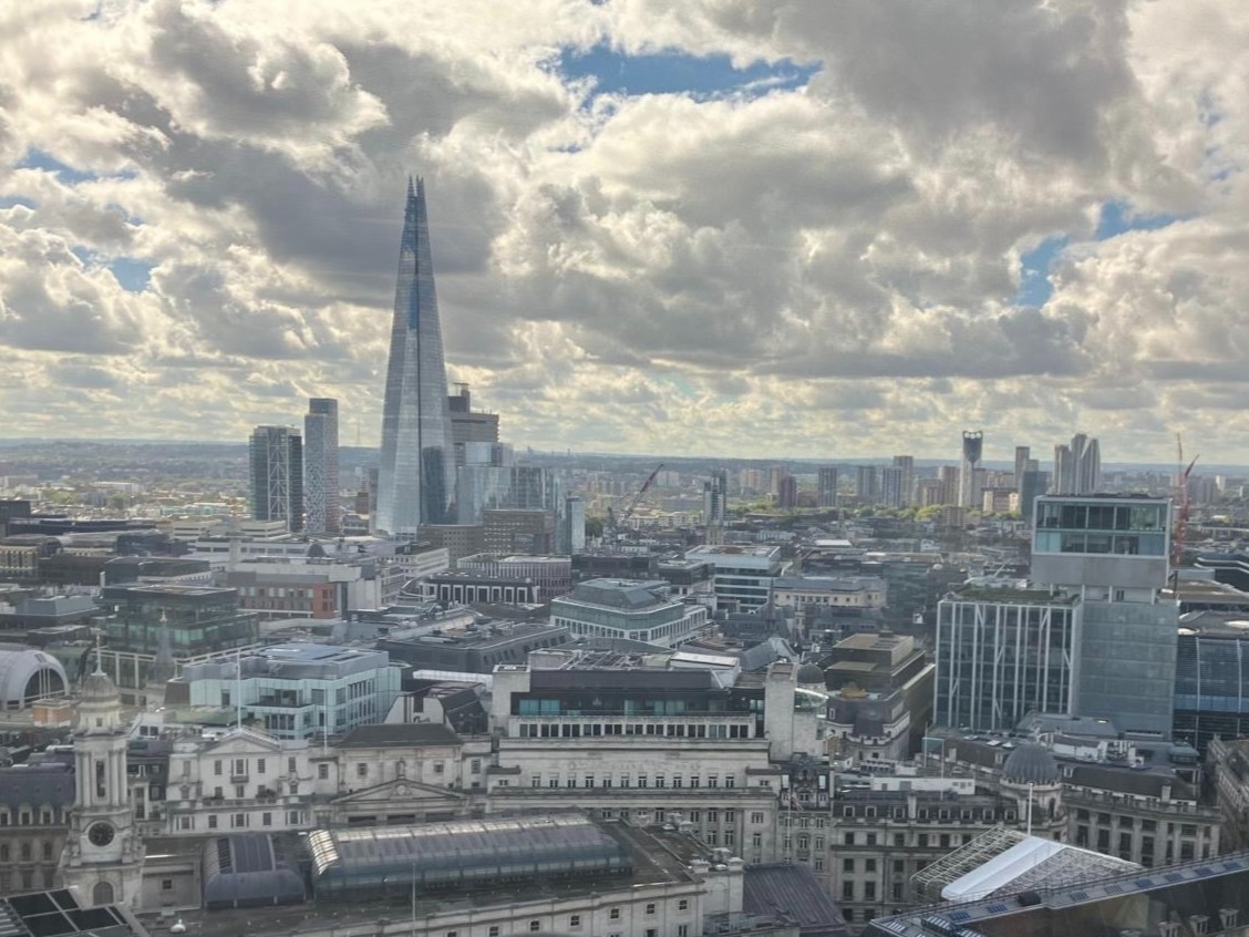 A cityscape of London featuring the Shard building under a partly cloudy sky.