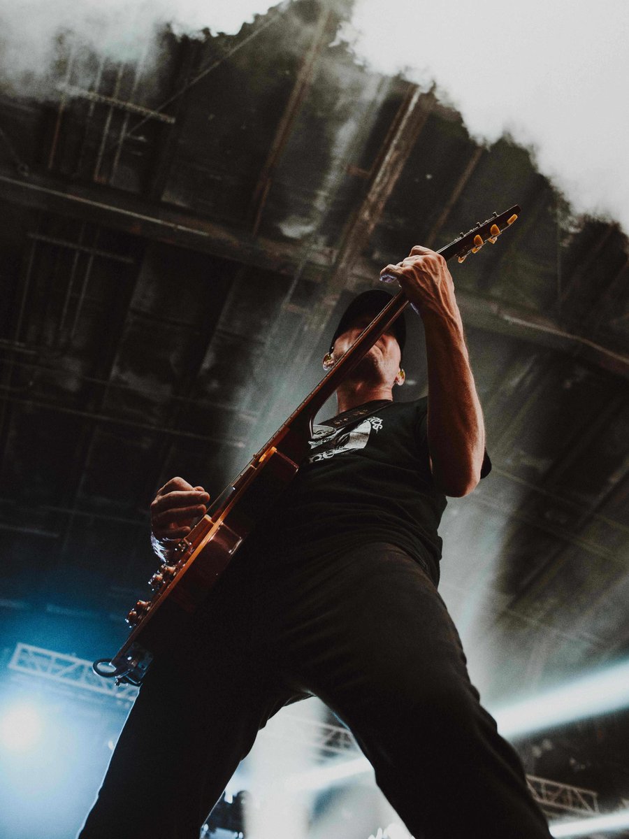 Guitarist playing guitar on stage with overhead lighting and smoke.