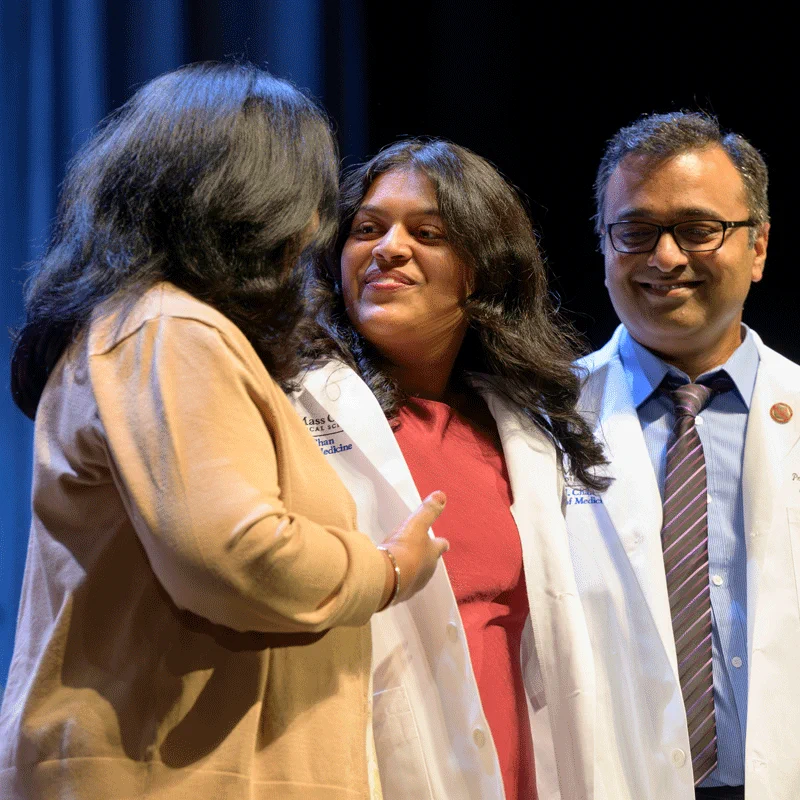 Coated student on stage with mom and mentor