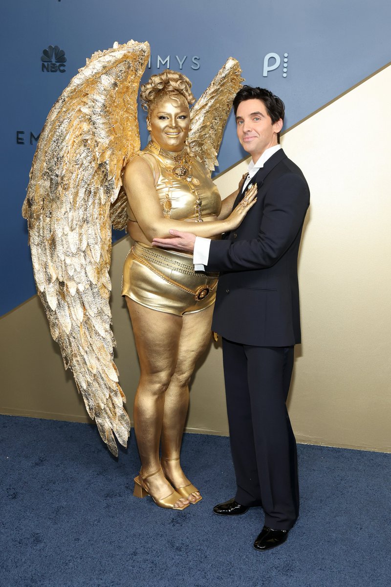 JustJared's tweet photo. Megan Stalter dressed up as an #Emmys statue while arriving at the 2026 ceremony with "Hacks" co-star Paul W Downs. 
#MegStalter
#PaulWDowns
#Hacks
#Emmys2026
Photos: Getty https://t.co/RQaVZvRdYp