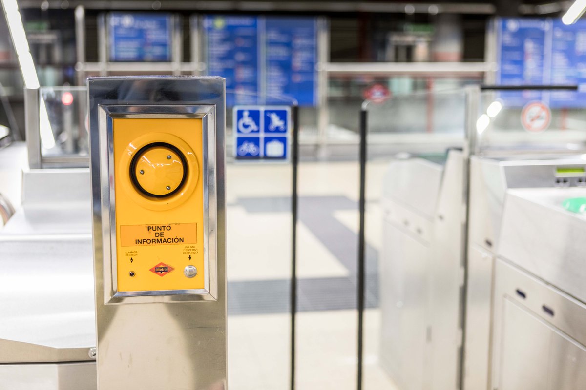 Un interfono amarillo ubicado junto a los tornos de entrada a una estación de metro.
