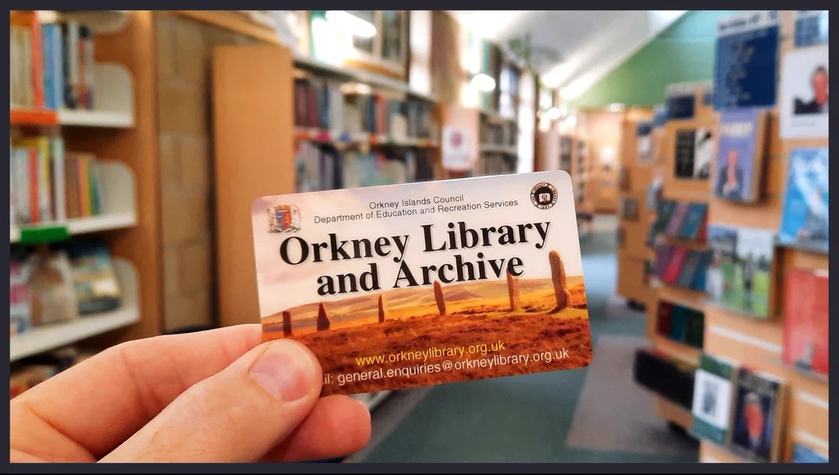 An Orkney Library card in front of library bookshelves