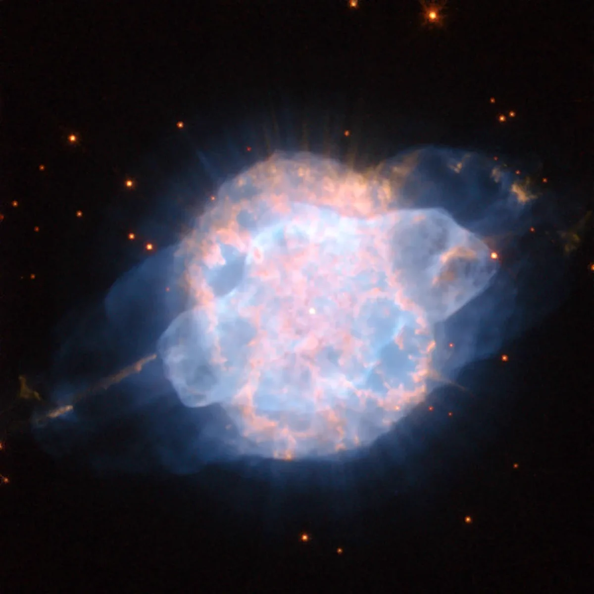 A nebula glows in bright shades of pink and blue, forming a multilayered blob that shines against black space, dotted with orange stars.
