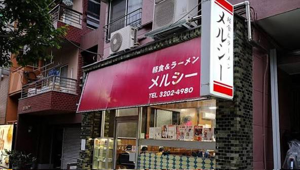 chiki__0125's tweet photo. メルシーとかいう最高の早稲田大学商店街のラーメン屋について

早稲田大学にはメルシーというラーメン屋がある。

正確には早稲田大学ではない。大学の外、馬場下町にある。でもこういうものを「大学の外」と呼ぶから近代大学はおかしくなる。メルシーは早稲田大学です。 少なくとも早稲田大学史を書くなら、総長と教授会と学生運動だけ書いてメルシーを書かないのは、人体解剖図から胃を抜くようなものだと思う。

1958年創業。しかも店主のお父さんは戦前から早稲田界隈で喫茶店をやっていた。開店して数年で戦争になり店を閉め、戦後は進駐軍のもとでハンバーグを作る仕事をして、1958年に早稲田へ戻ってメルシーを開いたという。

何その経歴。

戦前早稲田の喫茶店→戦争→ 占領軍のハンバーグ屋→ 戦後早稲田のラーメン屋

一軒の食堂の経歴だけで昭和史が一周している。

創業当時はラーメンだけではなく、コーヒー、丼、サンドイッチ、かき氷まで出していたらしい。「軽食＆ラーメン」という看板が今見ると妙なのだが、たぶん何屋かという問い自体が間違っている。

早大生を食わせる屋である。

大学というと、みんな大隈重信とか建学の精神とか学問の独立とかを語りたがる。でも学生は理念だけでは午後の授業まで生きられない。朝からベンサムとかミルを読んでも十二時半には腹が減る。戦後民主主義について三時間議論しても腹が減る。大学自治を守っても腹が減る。

思想には左右があるが、腹には昼がある。

そこでメルシーがラーメンを出す。

これが大学でなくて何なのか。

しかも1970年に現在地へ移転してから半世紀以上、味を大きく変えずにやってきたという。大学の建物は建て替わる。先生は退職する。学部は再編される。学生運動は終わる。入試制度も変わる。キャンパスには新しい建物が生えて、昔の学生が戻ってくると「ここ何だったっけ」となる。

なのにメルシーへ行くとラーメンが出てくる。

大学本体よりバージョン管理が厳格である。

しかも昔の学生が何十年後に戻ってきて食べる。「学生のころ食べた味だ」と言う。横では今の学生が同じものを食っている。

これ、ほとんど典礼では？

1958年の学生が食う。
1968年の学生が食う。
1988年の学生が食う。
2008年の学生が食う。
2026年の学生が食う。

教員は全員入れ替わっているのに、煮干しと醤油だけが使徒継承している。

早稲田大学の共同体とは何か、と聞かれたら、学生証を持っている人の集合だけではないと思う。もう死んだ卒業生もいる。まだ入学していない高校生もいる。昔そこで本を売った古本屋も、三品で飯を作った人も、喫茶店で学生の議論を聞いていた人もいる。

そしてラーメンを作った人がいる。

2024年、メルシーが人手不足で一時休業したとき、早稲田界隈がざわついたのも面白い。普通なら一個人経営の飲食店が休むだけである。でも常連や学生が「えっ」となる。

そりゃそうだ。

自分の記憶の保存施設が突然閉まったからである。

しかもその後、常連や学生らの力もあって営業を再開した。

これが最高なんですよ。

文化財指定されているわけではない。大学法人の施設でもない。早稲田大学から「本学の重要無形ラーメン文化財として保護します」と予算が降りるわけでもない。

でもみんな知っている。

なくなったら困る。

大学って、本当はこういう「なくなったら困る」の集合体なんだと思う。

図書館がなくなったら困る。先生がいなくなったら困る。古本屋がなくなったら困る。学生が集まる喫茶店がなくなったら困る。安く飯を食わせる店がなくなったら困る。

だから大学の境界線を正門で切るのはおかしい。

早稲田大学商店街という巨大な生態系があって、その中に大学法人早稲田大学が入居している、と考えたほうが実態に近いのではないか。

大学本体がCPUなら、古本屋は外部記憶装置、喫茶店は通信設備、三品は電源、そしてメルシーはたぶん基礎代謝である。

偉い先生が思想を作る。

学生がそれを読む。

議論する。

腹が減る。

メルシーへ行く。

また大学へ戻る。

この循環を七十年近くやっている。

大学史の年表には「1958年　メルシー創業」と書いておいてほしい。

大隈重信が大学を作った。

その後いろんな人が大学を守った。

そして小林さんのお父さんはラーメンを作った。