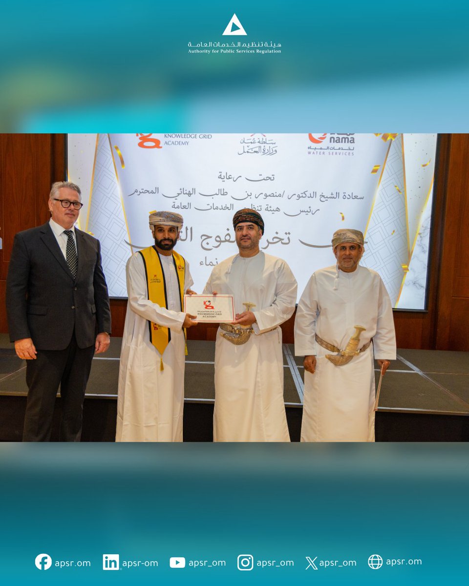 يقف أربعة اشخاص على منصة حيث يتبادل اثنان منهم شهادة تقدير أمام الحضور، بينما يقف الآخران إلى جانبهما. تظهر خلفهم شاشة تحمل عبارات.