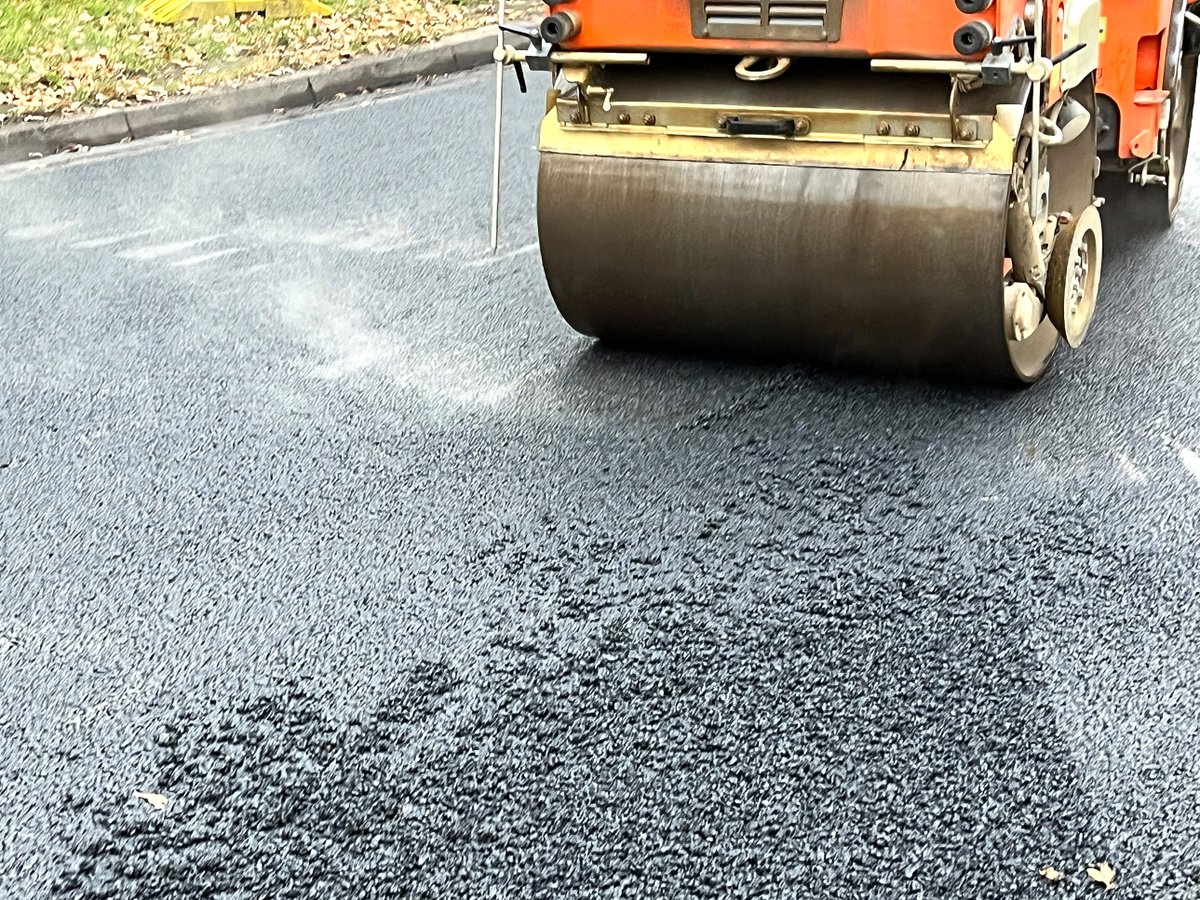 Ein Straßenwalzer fährt über eine frisch gepflasterte Straße und verdichtet den Asphalt.