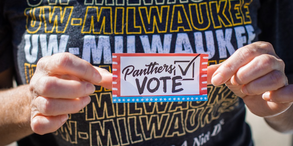 A person wearing a UW-Milwaukee t-shirt holds a "Panthers Vote" sticker.