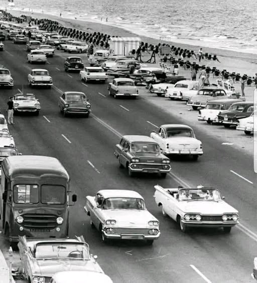 Anna15gw's tweet photo. A beach, a packed road, and nothing but classic cars…  What year do you think this photo was taken? https://t.co/lhruNdLtMJ