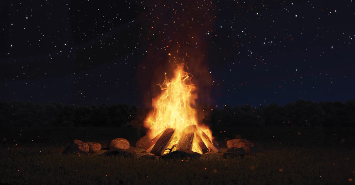A large fire burns brightly in the centre of a circle of rocks. The fire's glow illuminates the area around it against a starry night sky.