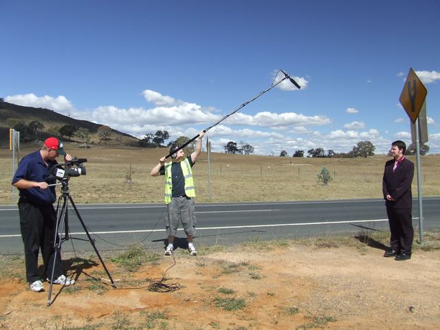 A photo of a cameraman, a presenter and a boom operator holding a microphone on a pole above the presenter so it's not visible in the shot.