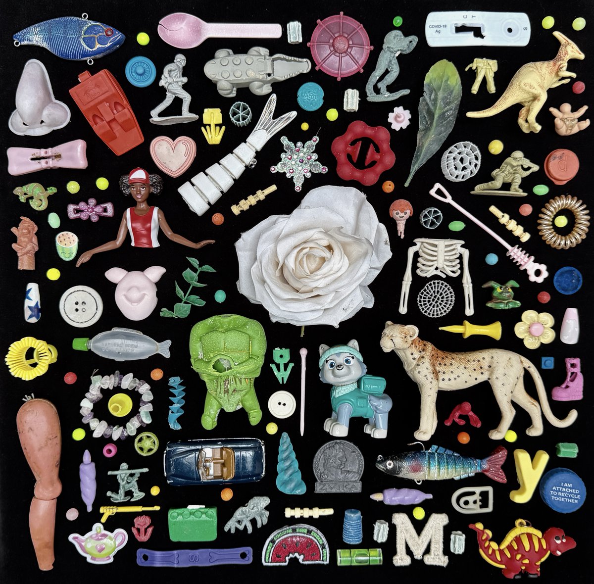 Miscellaneous beach finds laid out on a black background. Among the colourful finds featured are false nails, finger prickers, toy soldiers, toy animals, fake flowers and foliage, a plastic nose, Lego, a soy sauce fish and a covid test kit.
