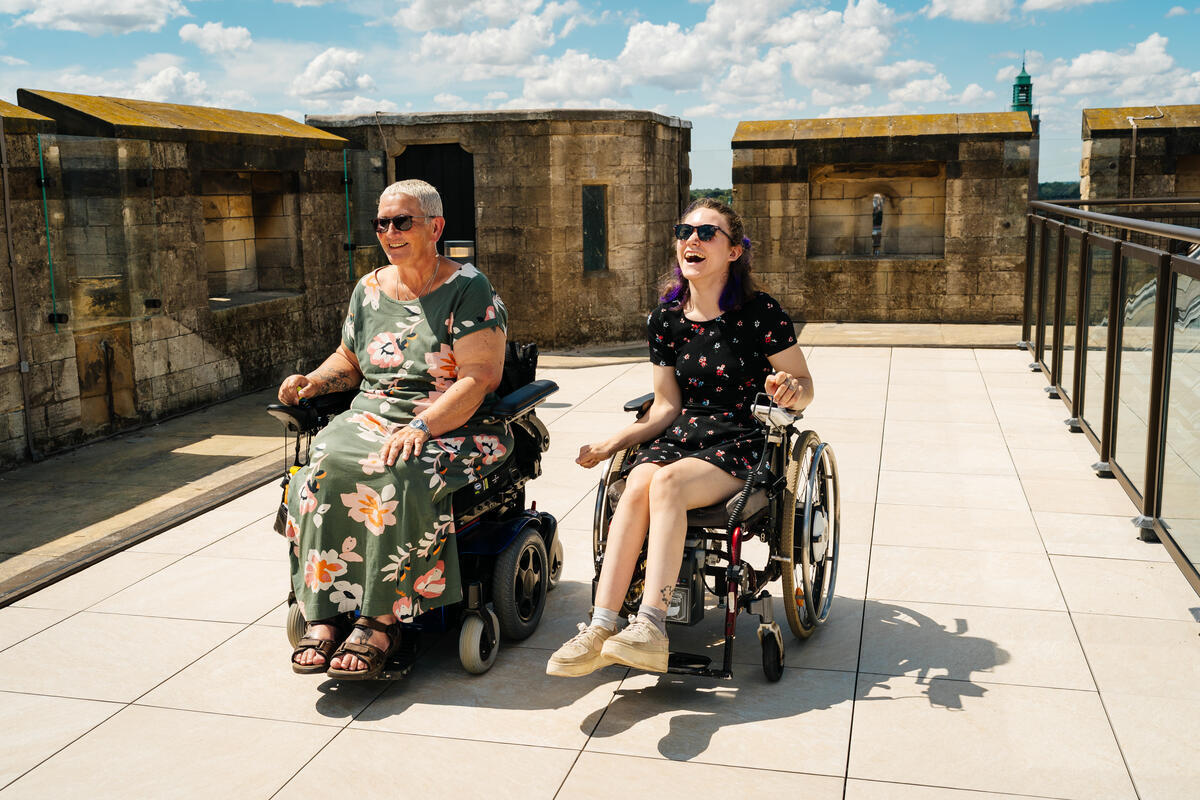 Two smiling ladies in wheelchairs enjoy the view from the battlements at Norwich Castle Keep at Norwich Castle, in Norfolk, England. Credit: Norfolk County Council/Norfolk Museums Service