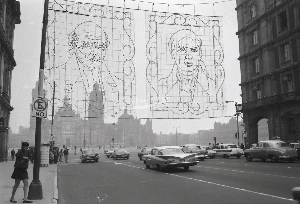 mexdeayer's tweet photo. Imagen de una luminaria decorativa con los rostros de Miguel Hidalgo y José María Morelos, instalada sobre la avenida 20 de Noviembre, en las inmediaciones del Zócalo capitalino de la Ciudad de México, con motivo de las fiestas patrias de septiembre.
La fotografía, tomada durante la década de los años sesenta, nos permite apreciar el ambiente que se vivía en aquella época en el primer cuadro de la capital, con el constante tránsito de vehículos y los históricos edificios que rodeaban esta emblemática zona.
La iluminación y decoración del Zócalo durante las fiestas patrias se convirtió, con el paso de los años, en una tradición que anunciaba la llegada de septiembre y llenaba de color las calles del Centro Histórico. Generación tras generación, habitantes y visitantes han disfrutado de estas decoraciones que forman parte de los recuerdos de la Ciudad de México.

AGN