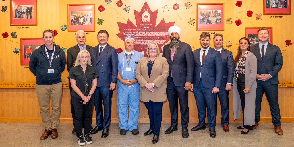 Group of eleven people standing in front of a yellow wall decorated with red maple leaves and framed photos, posing for a formal photo.