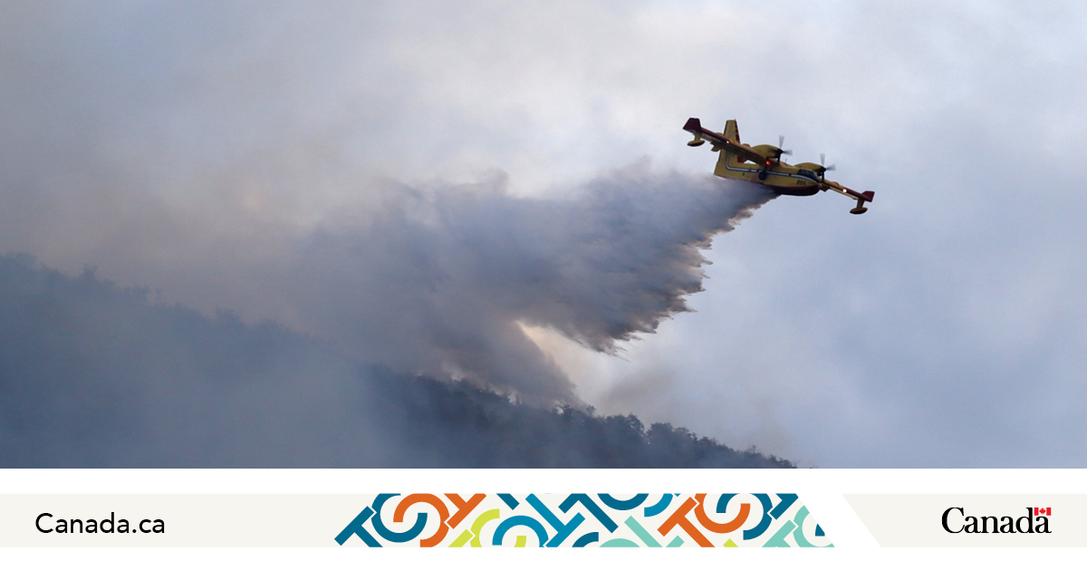 Firefighting aircraft dropping water from the sky while surrounded by smoke.