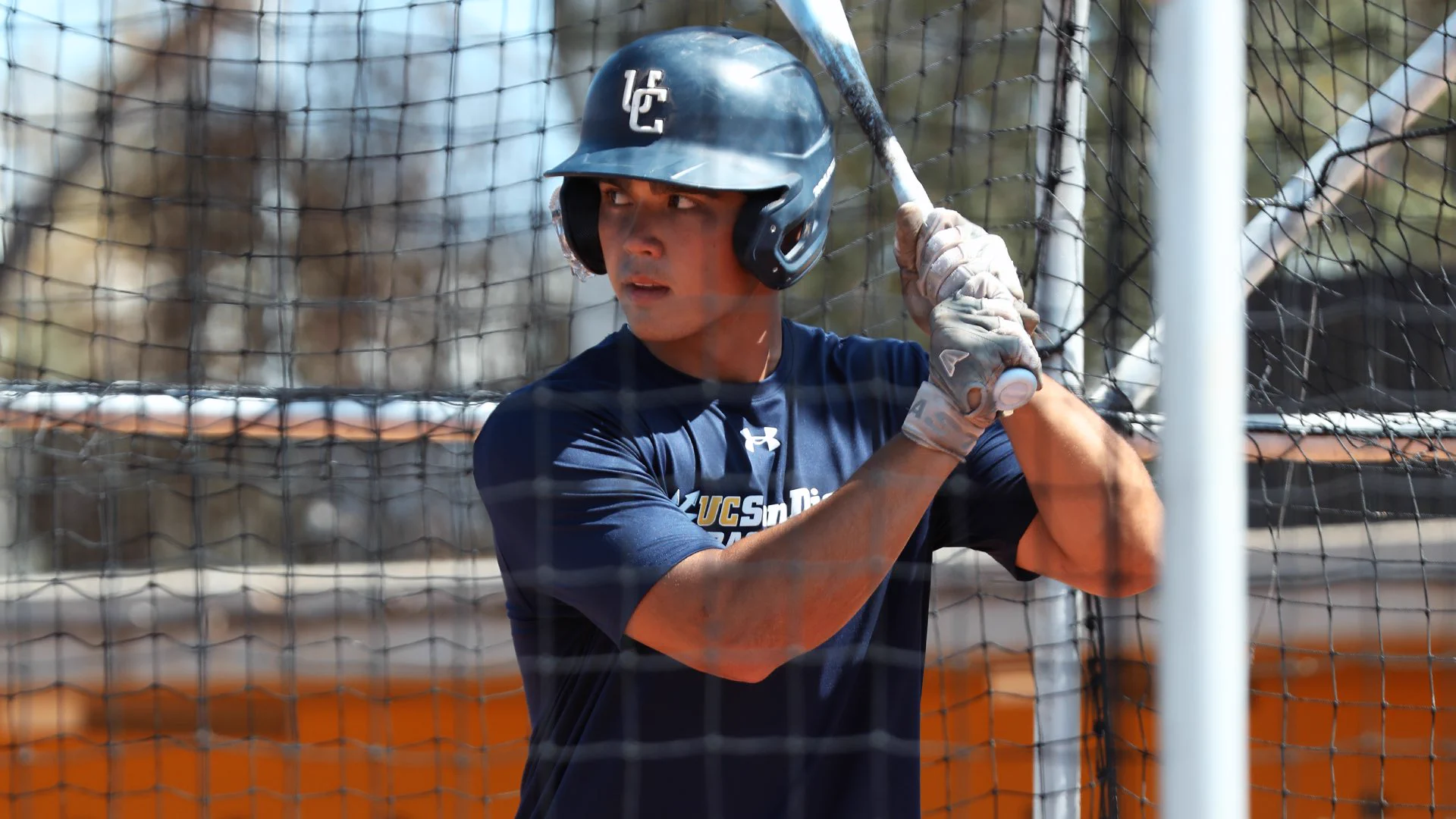 Baseball player with bat and helmet in batting cage