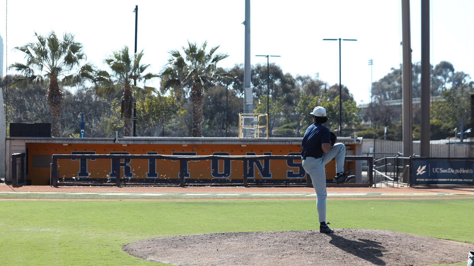 Pitcher throws on mound with “Tritons” in background