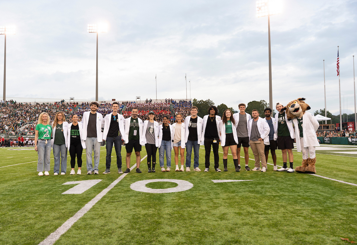 OUHCOM's tweet photo. On Saturday, #OUHCOM sponsored the game between the @OhioBobcats and Jacksonville State. Interim Senior Dean Jennifer Gwilym, D.O., and students stepped on the field to toss T-shirts and celebrate our 50th anniversary during an incredible fourth-overtime win. https://t.co/fCFm3pwiiz