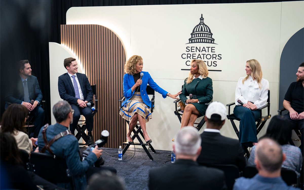 Panelists speaking on stage during a Senate Creators Caucus event in front of an audience.