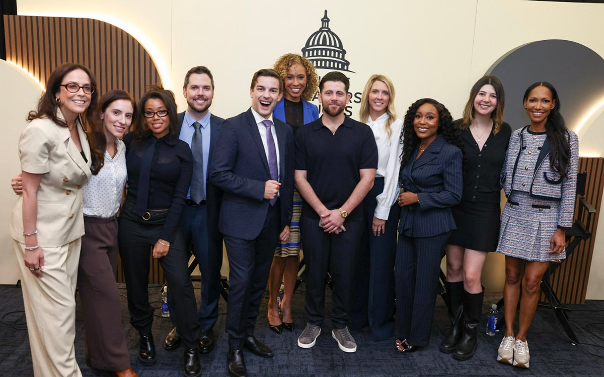 A group portrait of panelists and participants smiling together on stage beneath the Senate Creators Caucus logo.