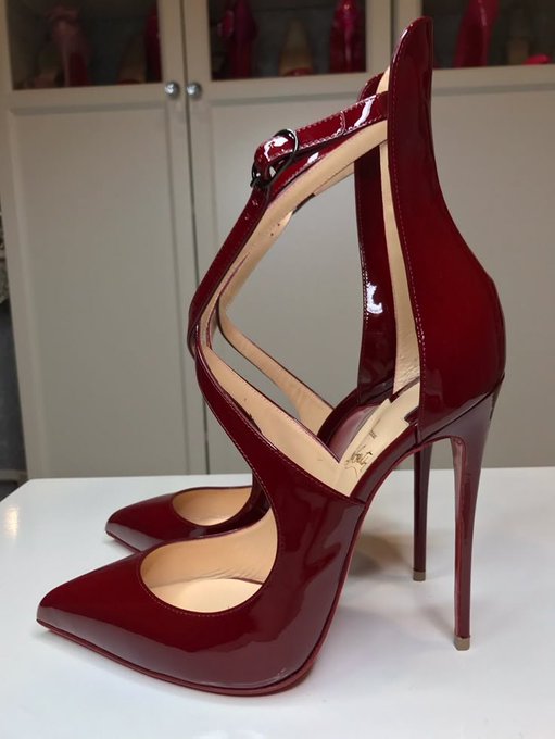 A photograph of a pair of dark red patent leather high-heeled shoes with pointed toes and cut-out designs, displayed on a white surface.