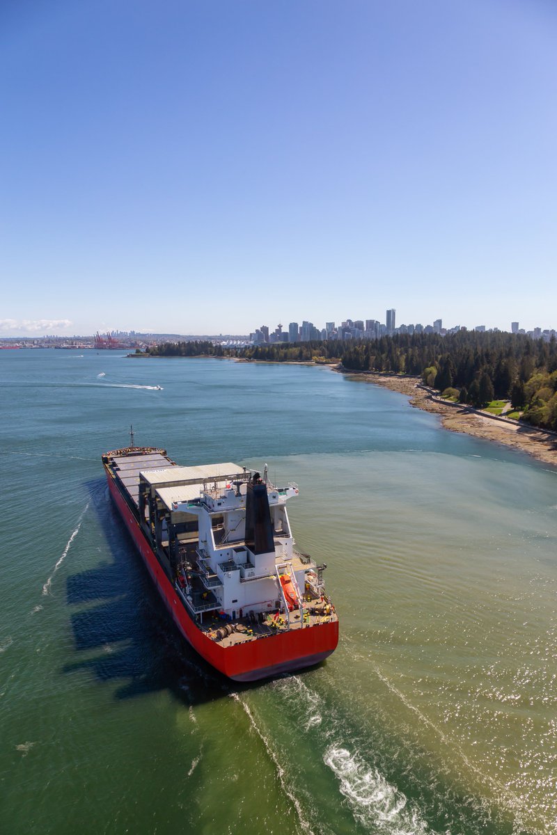 Aerial View of a Big Container Ship passing by Stanley Park with Downtown City in the Background. Taken from Lions Gate Bridge, Vancouver, British Columbia, Canada.