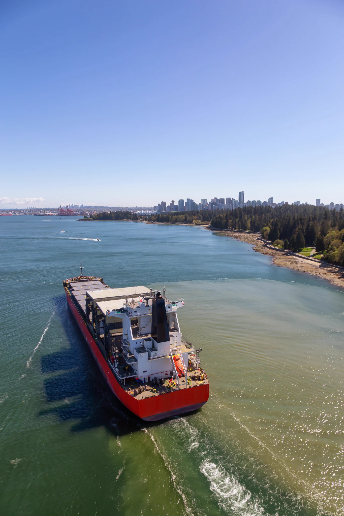 Aerial View of a Big Container Ship passing by Stanley Park with Downtown City in the Background. Taken from Lions Gate Bridge, Vancouver, British Columbia, Canada. 