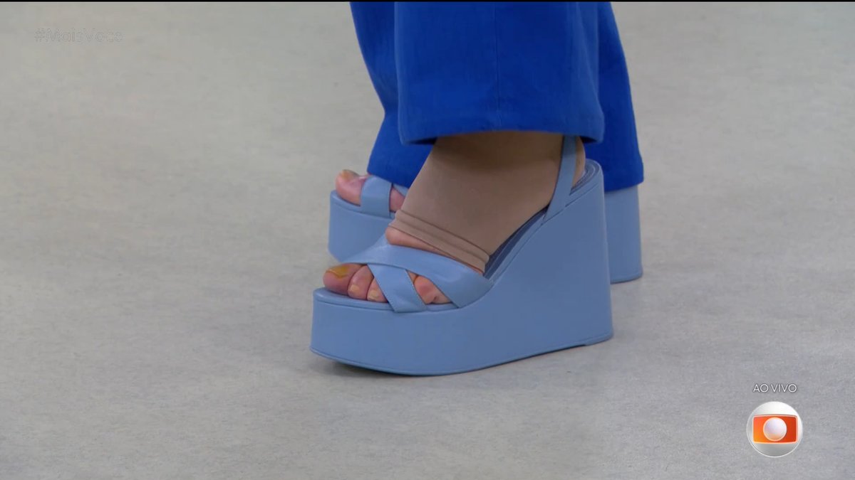 Close-up of a person wearing bright blue wedge platform sandals and matching blue pants, with a Globo network 'AO VIVO' (live) logo in the corner.