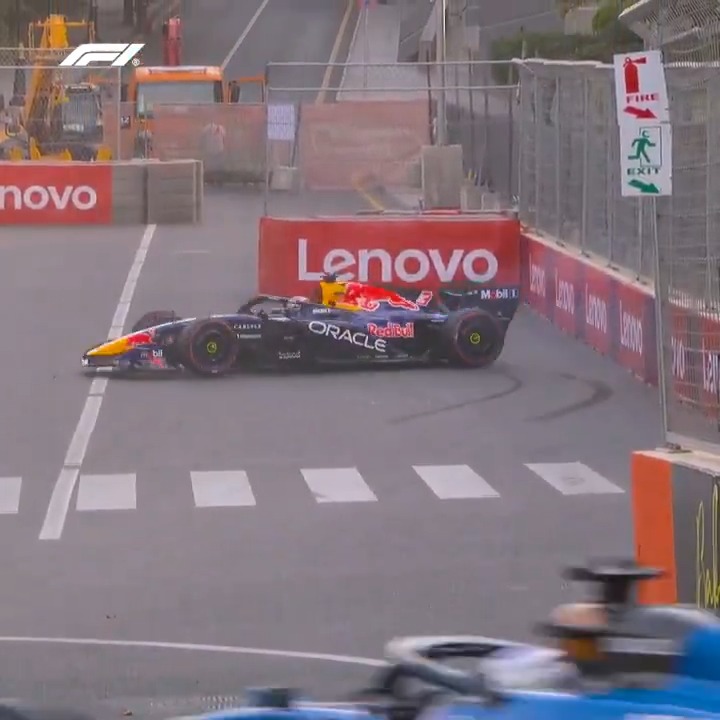 An F1 Red Bull Racing car, sponsored by Oracle, Mobil, and Carapelli, rejoins the track past a Lenovo barrier during the Azerbaijan Grand Prix. The image captures the moment the car spins back onto the circuit, with tire marks visible on the asphalt and an emergency exit sign nearby.