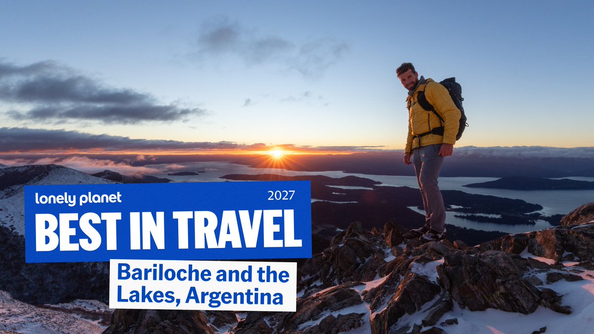 A hiker with a backpack stands atop a rocky, snow-dusted mountain peak at sunrise, overlooking the lakes and landscape of Bariloche, Argentina, with a banner reading "Lonely Planet Best in Travel 2027" highlighting the destination.