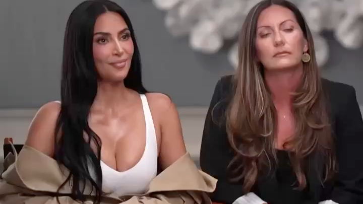 Kim Kardashian sits next to a woman with long brown hair in a black blazer on what appears to be a talk show set.