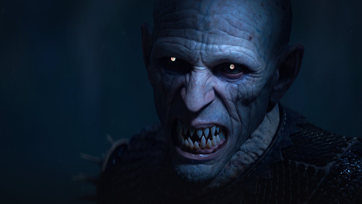 A terrifying, wrinkled, bald-headed man with many sharp pointed teeth and glowing eyes, leers towards the camera. It is the vampire Brencis from The Blood of Dawnwalker.