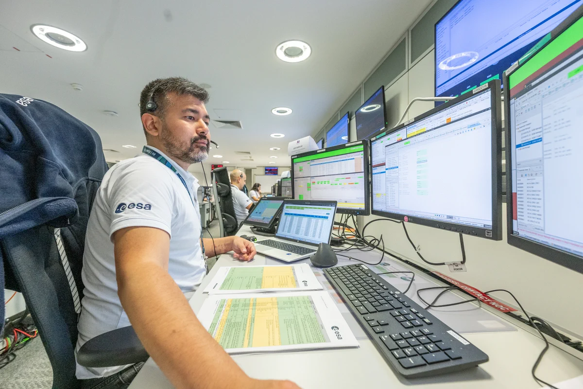 Federico Ferre, Data Handling Engineer at ESA, sits at a workstation at ESA’s European Space Operations Centre (ESOC) during the launch and early orbit phase (LEOP) for Copernicus Sentinel-3C.


Federico is wearing a headset works at a multi-screen workstation, monitoring spacecraft operations data, schedules, and system status displays. Printed procedures, a laptop, and several monitors are arranged across the desk, while additional operators and wall-mounted displays are visible in the background of the mission operations room.